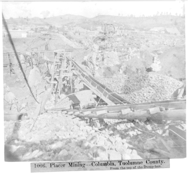 Ein Schwarz-Weiß-Foto eines Kohlebergwerks in Kolumbien, das ein paar Gebäude, Bäume und Berge im Hintergrund zeigt, mit Text unten.
