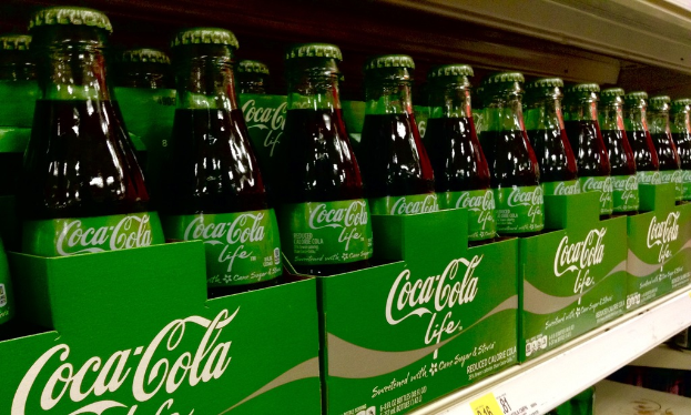 Glasflaschen werden in grüne Kartons mit 'Coca-Cola Life' darauf gestellt.