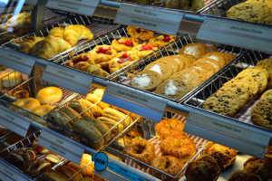 Ein Bäckereischaufenster voller verschiedener Keks- und Kuchensorten, Cookies und andere Backwaren, mit Schildern, die die Art der Backwaren angeben.