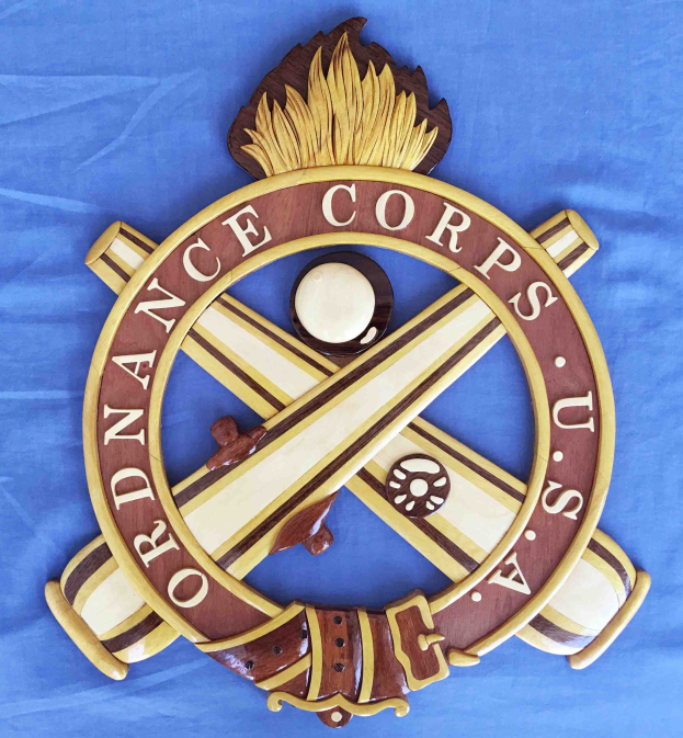 Holzschild mit "Ordnance Corps" in schwarzer Schrift, auf blauem Tuch montiert, mit einem weißen Stern auf marineblauem Hintergrund mit goldener Umrandung, umgeben von kunstvollen Verzierungen.