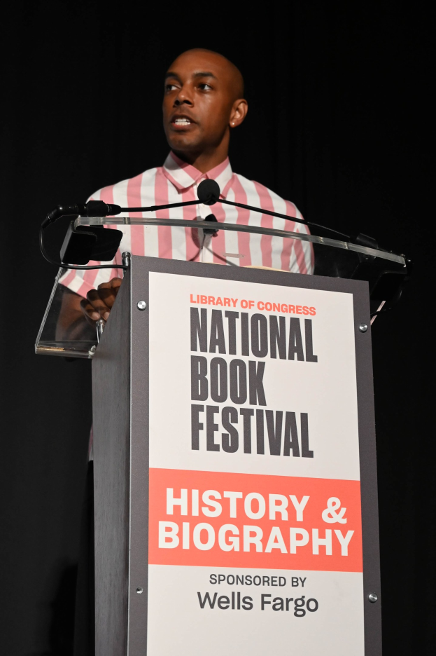 Mann spricht an einem Rednerpult mit einem Mikrofon während eines Abendveranstaltung, mit einem "National Book Festival History & Biography"-Schild dahinter.