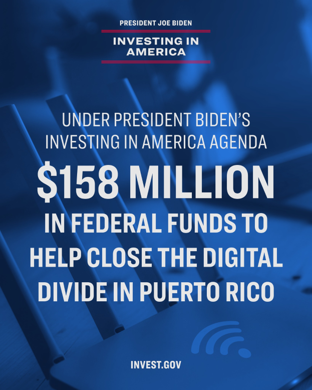 Ein Plakat mit Text über das Investing in America-Agenda des Präsidenten Biden und 158 Millionen Bundesmittel für die digitale Kluft in Puerto Rico, mit einem Laptop, einem Stapel Papiere und einem Kaffeebecher auf einem Tisch davor.