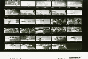 Ein Schwarz-Wei├č-Foto eines Mannes in einem wei├čem Hemd und Shorts, der einen Tennisschl├Ąger h├Ąlt und einen konzentrierten Ausdruck hat, mit einem Filmstreifen im Hintergrund.