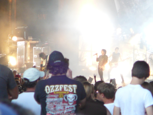 Eine Gruppe von Menschen in verschiedenen Kleidern, einige mit Mützen, in der Nähe von Musikinstrumenten einschließlich einer Gitarre und einem Mikrofon, mit Bühnenbeleuchtung.