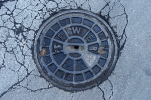 Ein Metallgulldeckel am Straßenrand mit Rissen und eingravierten Text.