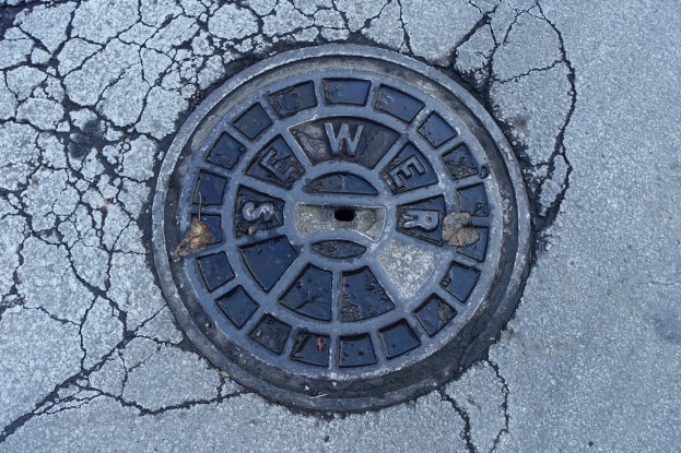 Ein Metallgulldeckel am Straßenrand mit Rissen und eingravierten Text.