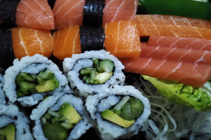 Ein schwarzer Teller mit verschiedenen Sushi-Stücken, darunter Lachs, Avocado und Gurke, umgeben von ein paar grünen Blättern.
