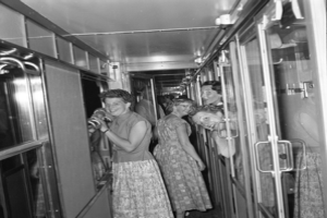 Eine Gruppe von Frauen, die auf einem Zug mit Türen auf beiden Seiten und Lampen oben steht, dargestellt in Schwarz-Weiß.