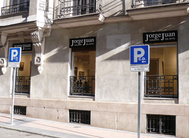 Ein mehrstöckiges Gebäude mit Fenstern, Geländern, Türen und Säulen, das Schilder an Pfosten entlang des Gehwegs und sichtbare Innenobjekte aufweist, die auf eine belebte städtische Umgebung hinweisen.