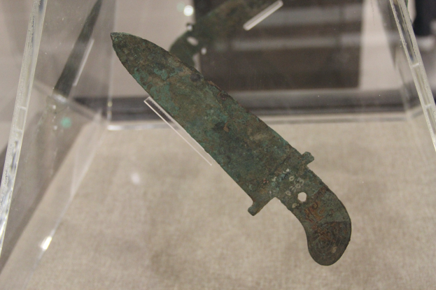 Ein Messer in einer durchsichtigen Glasvitrine, mit detaillierten Verzierungen auf der Klinge.