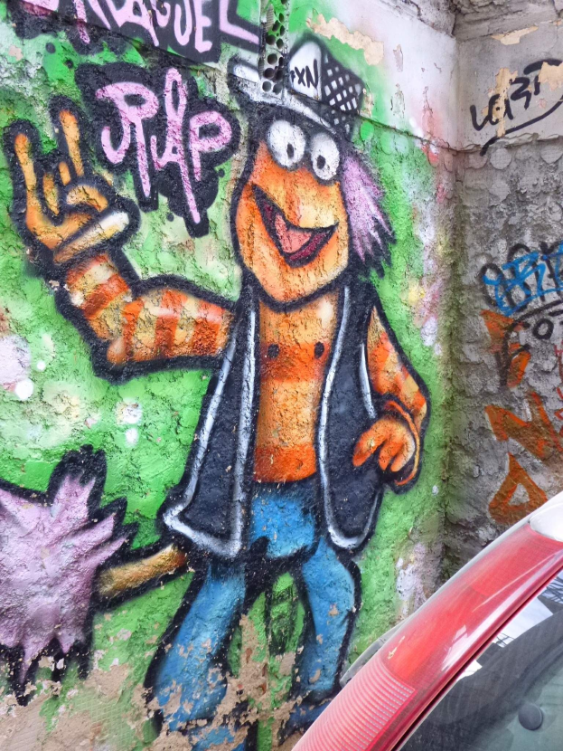Roter Wagen vor einer farbenfrohen Graffiti-Wand geparkt.