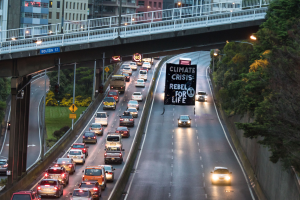 Eine belebte Stadtstraße mit starkem Verkehr, eine Brücke im Hintergrund und ein Banner in der Mitte der Straße.