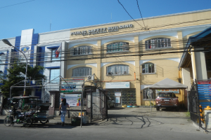 Gebäude umgeben von Bäumen, Straßeninfrastruktur, Fahrzeugen, Fußgängern und einem klaren Himmel.