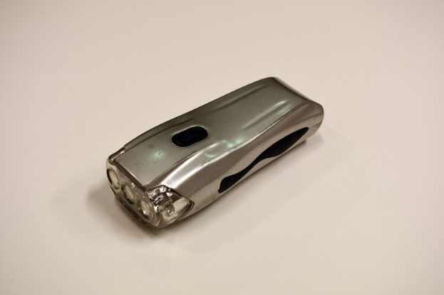 Ein silbergrauer Elektroschocker mit glänzender Metalloberfläche auf einem weißen Tisch.