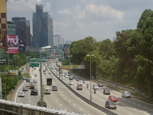 Eine vielbefahrene Autobahn mit hohen Gebäuden, Straßeninfrastruktur und Bäumen unter einem bewölkten Himmel.