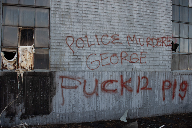 Ein Gebäude mit Graffiti, das "Polizei ermordet George Fuck 12 P19" lautet, mit Fenstern und verschiedenen Gegenständen vorne drauf.