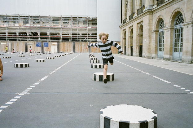 Vier Kinder sind in einem Schulhof mit schwarzen und weißen Zementstufen, ein Kind läuft auf dem Boden.