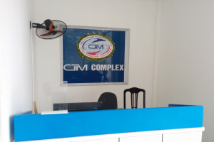 Ein blauer und weißer Empfangstisch mit einem Computer, umgeben von Stühlen und einem Tischventilator, mit einer Wandtafel, die Text und ein Logo anzeigt, das darauf hinweist, dass es das Büro von GM Trading Joint in Ho Chi Minh Stadt ist.
