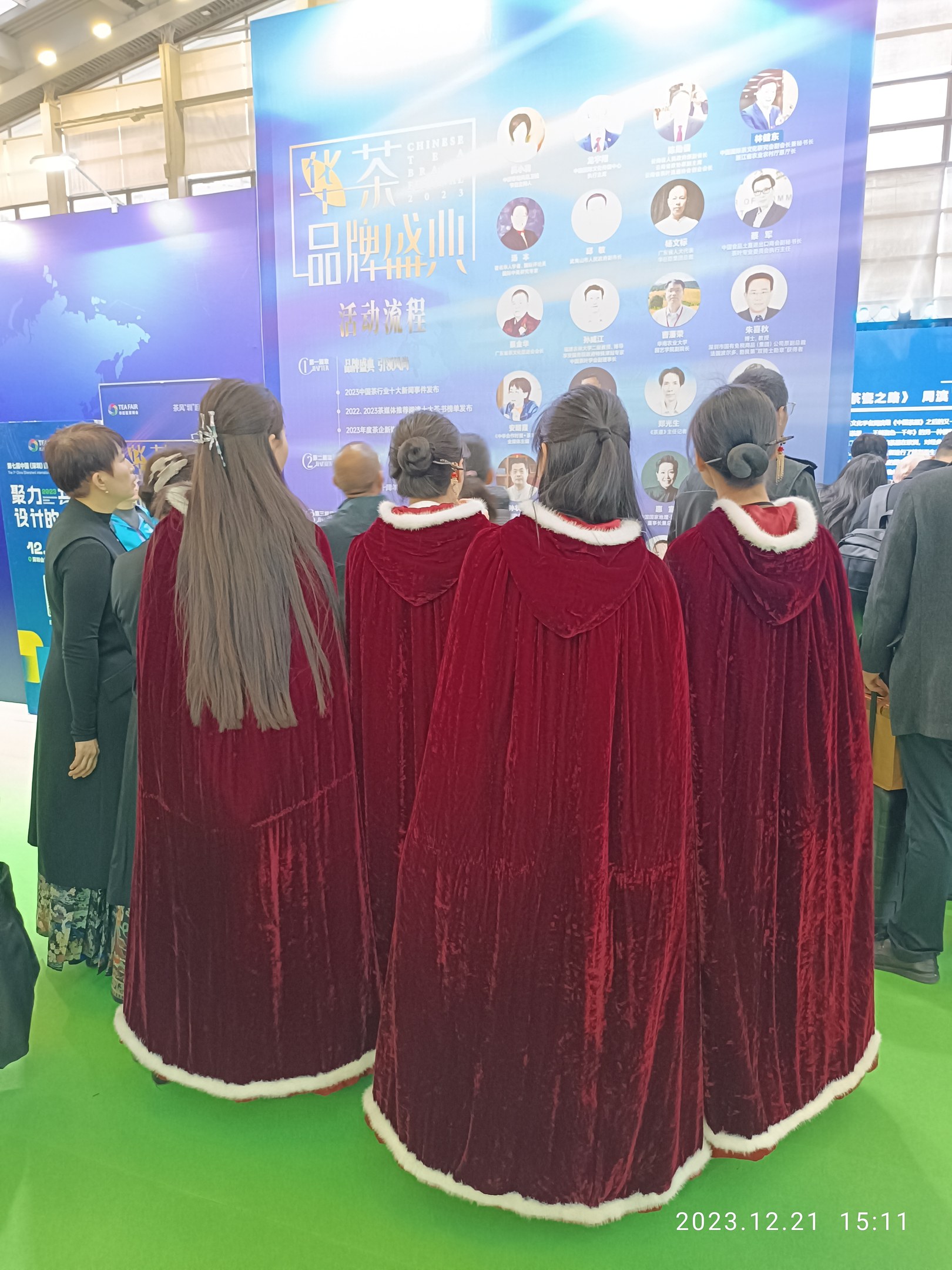 Eine Gruppe von Menschen in roten Kleidern steht auf einem grünen Teppich bei der China Tourism Expo 2019, mit Bannern, Lichtern und Glaswänden im Hintergrund.