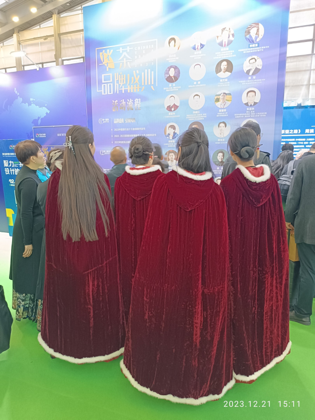 Eine Gruppe von Menschen in roten Kleidern steht auf einem grünen Teppich bei der China Tourism Expo 2019, mit Bannern, Lichtern und Glaswänden im Hintergrund.