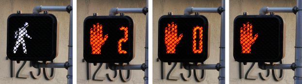 Eine Ampel mit drei Signalen an der Seite eines Gebäudes angebracht, mit einer Wand im Hintergrund.