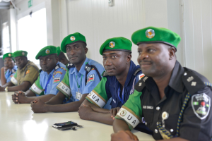 Gruppe von Polizeibeamten bei einer Schulung an einem Tisch sitzend, mit Mobiltelefonen und anderen Gegenständen auf dem Tisch, in einem Raum mit Fenstern und Deckenbeleuchtung.