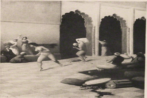 Schwarze und weiße Zeichnung einer Gruppe von Menschen in einem Raum mit einer Wand und Säulen im Hintergrund, betitelt mit "Gustav Klimt - Der Tanz der Nymphen".