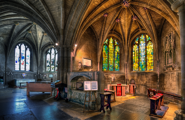 Ein Raum mit Bänken, Tischen, einer Tafel, Fenstern, einer Wand, Kerzen und einem Kamin, bearbeitet.