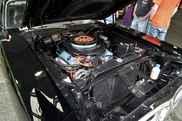 Nahaufnahme von Autokühlerteilen mit unscharfen Menschen und einer Straße im Hintergrund.