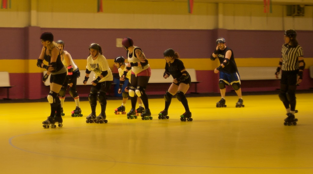 Menschen in Kleidung skaten auf einem Boden mit Bänken vor einer Wand.