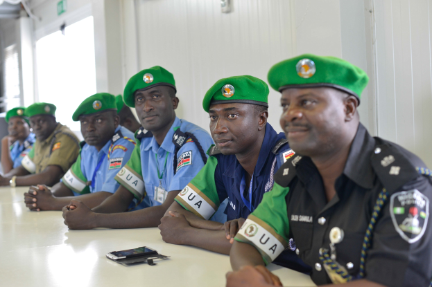 Gruppe von Polizeibeamten, die an einem Tisch während einer Schulung sitzen, mit Mobiltelefonen und anderen Gegenständen auf dem Tisch, in einem Raum mit Fenstern und Deckenlampen.