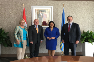 Eine Gruppe strahlender Menschen um einen Tisch mit Papieren, umgeben von Fahnen, Topfpflanzen und einem Foto auf der Wand, feiert die Unterzeichnung eines Memorandums zwischen den Vereinigten Staaten und Kanada.