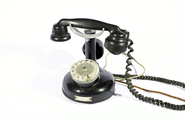 Ein schwarzes Telefon mit Zahlen und Text, der durch die Glasfläche sichtbar ist, verbunden durch Drähte, vor einem weißen Hintergrund.