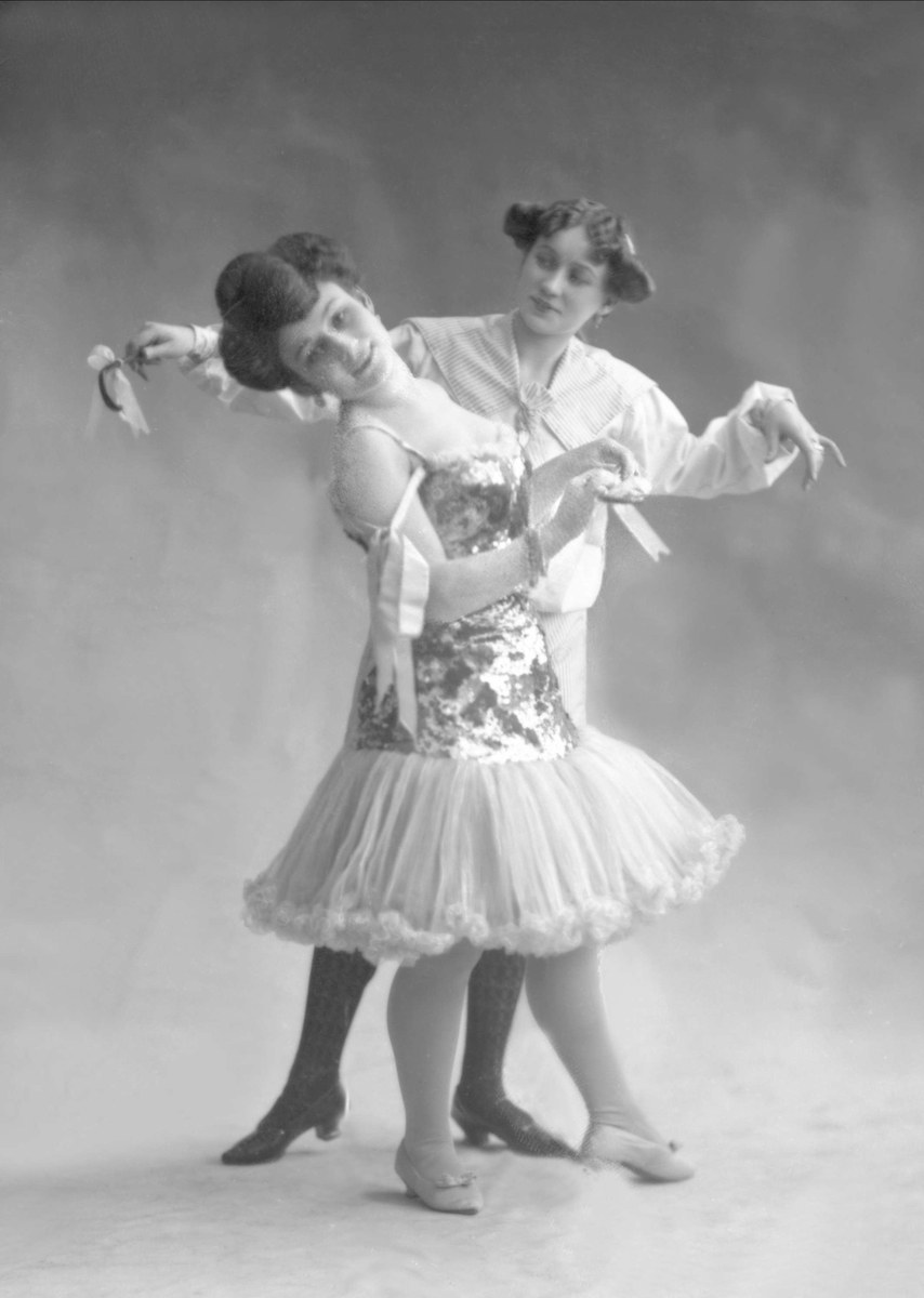 Zwei Frauen in einem Schwarz-Weiß-Foto tanzen synchron, eine hält ein Band, trägt Kleider.