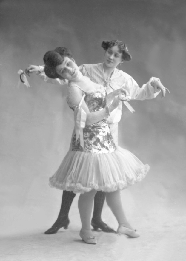 Zwei Frauen in einem Schwarz-Weiß-Foto tanzen synchron, eine hält ein Band, trägt Kleider.