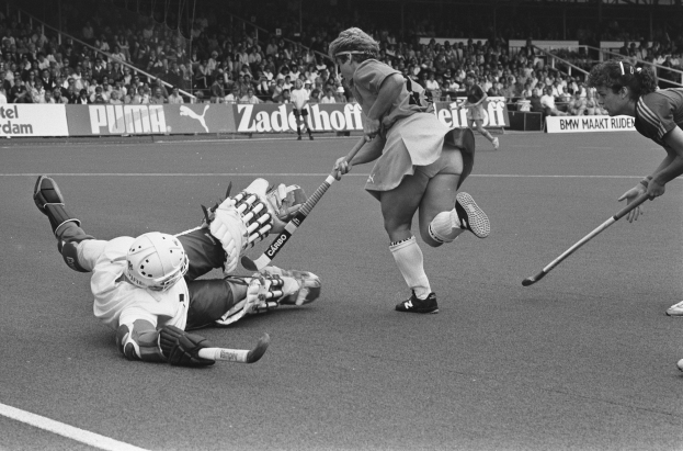 Schwarz-weißes Bild von Frauen, die Feldhockey in einem Stadion mit Zuschauern auf den Rängen spielen.