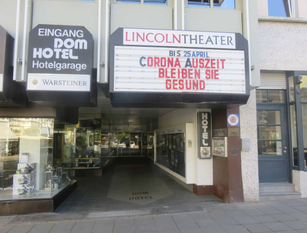 Das Lincoln Theater in Berlin, Deutschland, ein Gebäude mit Glasfenstern und -türen und einer Tafel mit Text darauf, das verschiedene Objekte im Inneren zeigt und so den Eindruck einer pulsierenden Stadtkulisse vermittelt.