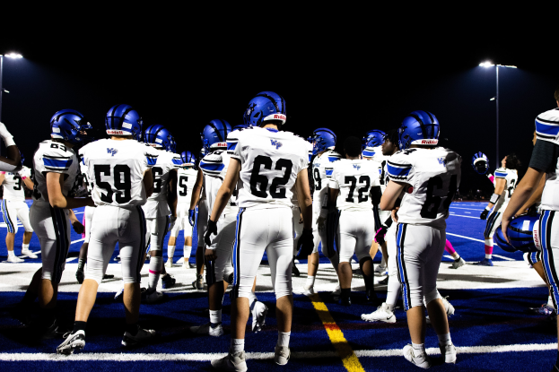 Eine Gruppe von Fußballspielern in Helmen und Stollenschuhen steht auf einem Feld, mit Flutlichtmasten im Hintergrund.