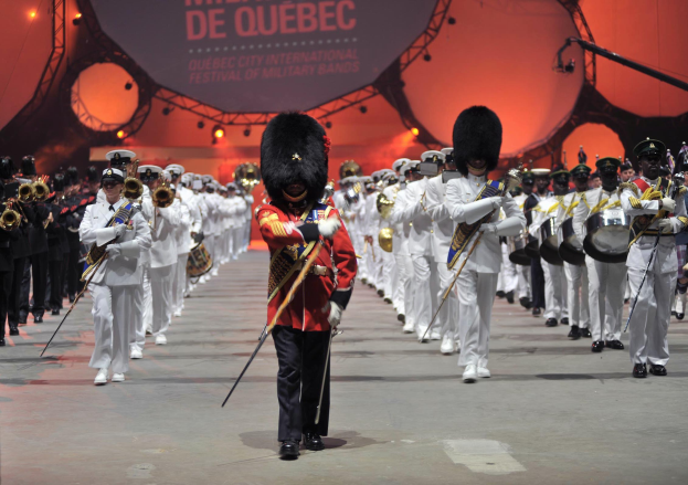 Eine Gruppe uniformierter Personen marschiert während der Eröffnungszeremonie des Montreal International Festival of Military Bands die Straße entlang und spielt dabei Musikinstrumente.