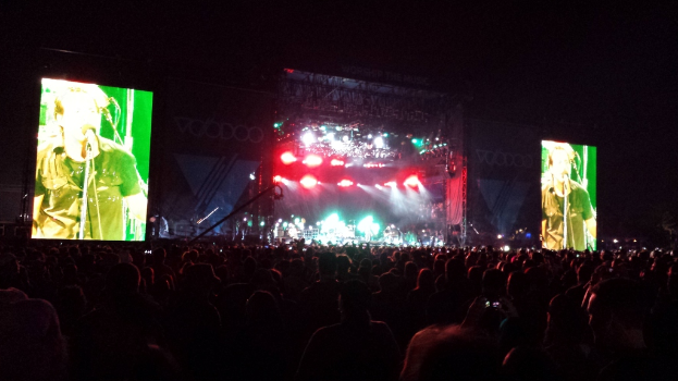 Eine Konzertszene mit einer Menge unten, einem großen Bildschirm links und einem kleineren Bildschirm rechts.