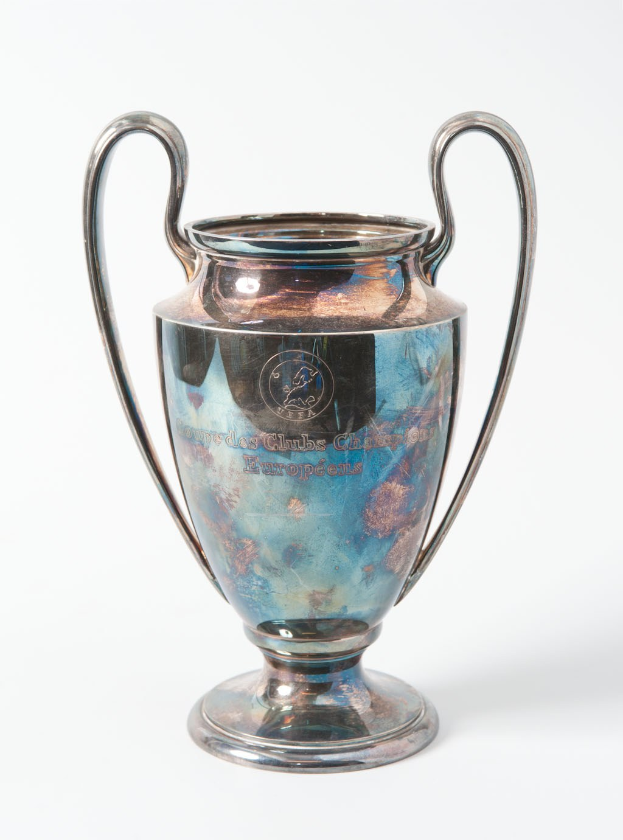 Der UEFA-Champions-League-Pokal, ein stählerner Becher mit zwei Griffen und einem blauen und silbernen Farbschema, der mit 'UEFA Champions League' beschriftet ist, vor einem weißen Hintergrund.