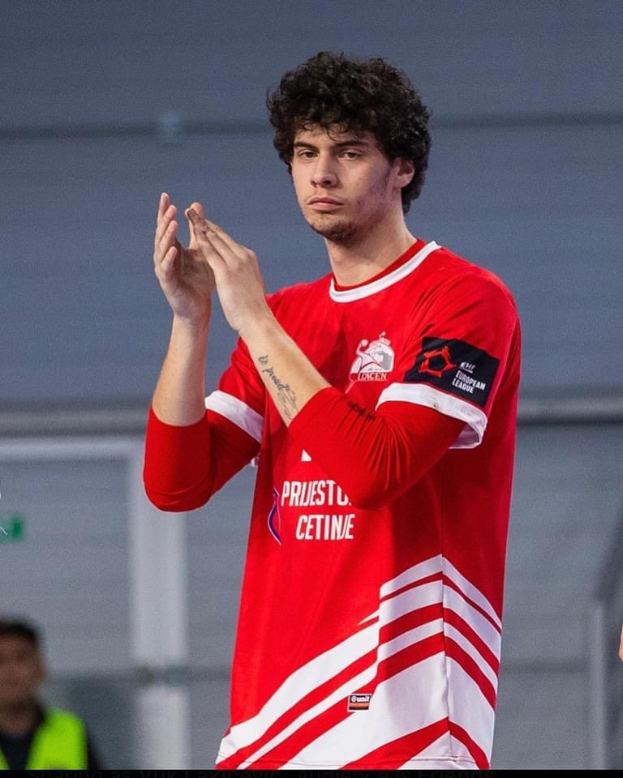 Ein Mann in einem roten und weißen Hemd klatscht in den Händen in der Vordergrund mit einer anderen Person und einer Wand im Hintergrund, mit Text, der unten links 'Kopenhagen Futsal Club - Foto 1' liest.