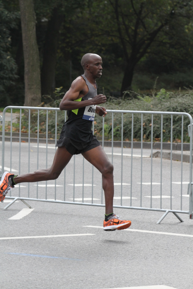 Ein Mann läuft bei einem Marathon auf einer von Bäumen gesäumten Straße, trägt sportliche Schuhe.