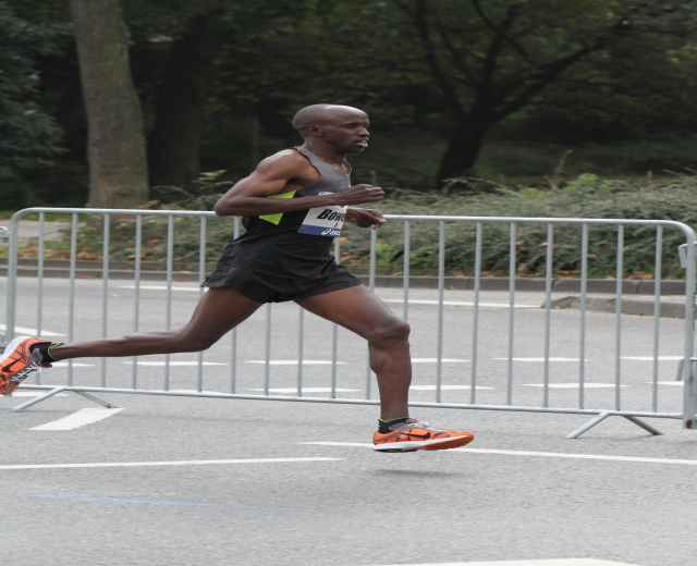 Ein Mann läuft bei einem Marathon auf einer von Bäumen gesäumten Straße, trägt sportliche Schuhe.