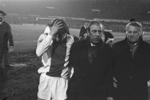 Eine Gruppe frustrierter Männer in Schwarz-Weiß-Kleidung steht zusammen auf einem Fußballfeld, mit einem Stadion im Hintergrund, wahrscheinlich nach einem gewonnenen Spiel.