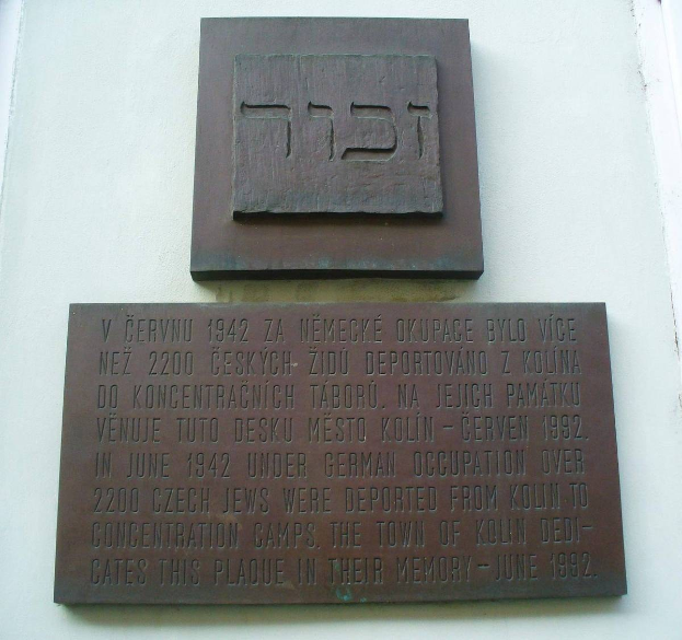 Metallplatte an einer Gebäudewand mit hebräischer Schrift, wahrscheinlich ein Denkmal für jüdische Gemeindeglieder.