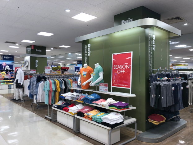 Ein Bekleidungsgeschäft mit Schaufensterpuppen umgeben von Kleiderstangen und Texttafeln, mit einem sichtbaren Boden und einer Decke mit Beleuchtung, Teil des ersten Geschäfts der Daiz-Marke in Singapur.