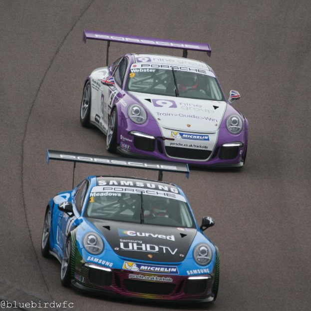 Zwei Autos fahren auf einer Straße außerhalb einer Stadt mit Text in der unteren linken Ecke.