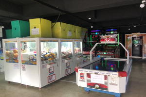 Ein Raum voller verschiedener Arcade-Spiele, mit einem Spielautomaten auf der rechten Seite, einem sichtbaren Boden und einer Decke mit Deckenbeleuchtung.