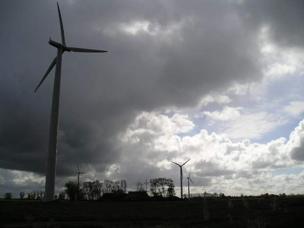 Windmühlen in einer Landschaft mit Bäumen, Wolken am Himmel und einem Haus in der Ferne.